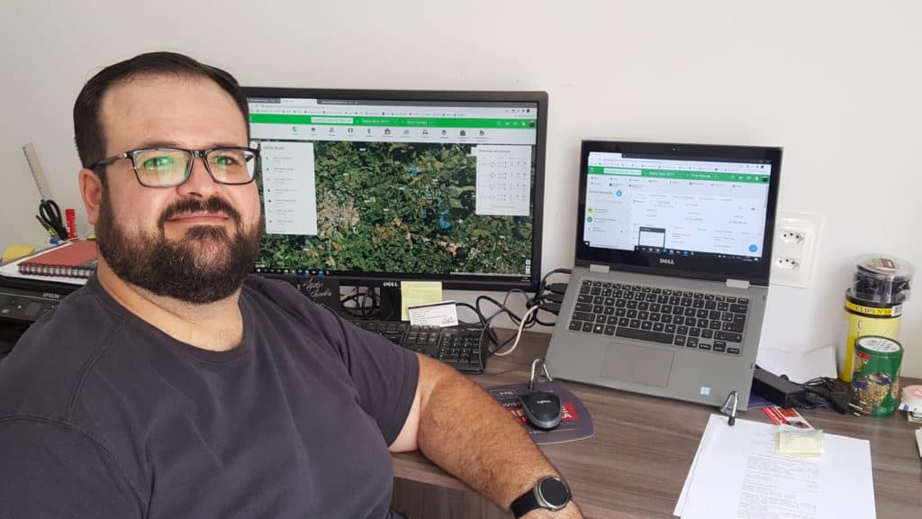 foto do consultor financeiro Alexandre Coser sentado em sua mesa de escritório com notebook e monitor abertos no Aegro