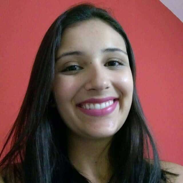 Foto da autora Mariana, sorrindo com uma parede vermelha no fundo