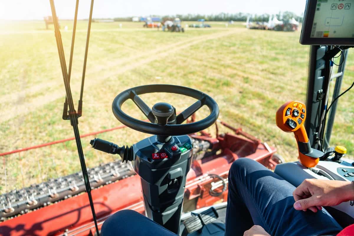 Foto de lavoura vista de dentro de um trator agrícola. É possível ver o volante e as pernas de quem comanda a máquina