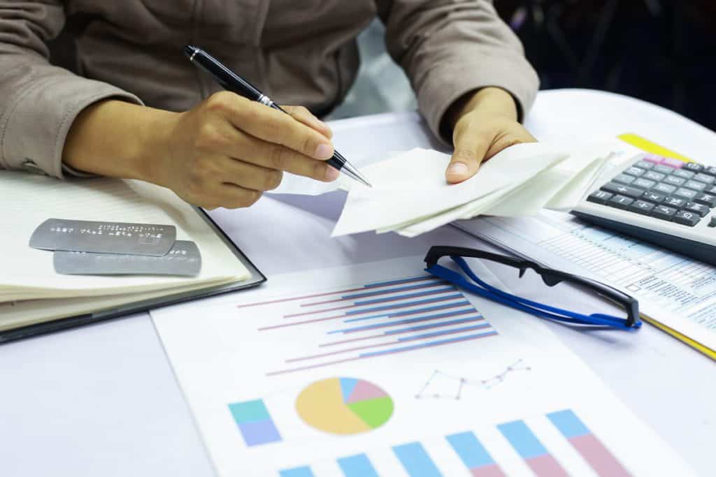 Pessoa em mesa de escritório, fazendo cálculos e olhando gráficos