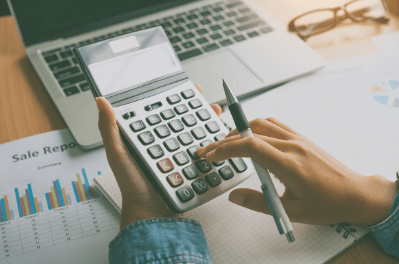 Pessoa usando uma calculadora sobre documentos e um laptop, trabalhando na EFD-Reinf.
